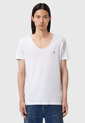 T-shirt blanc à manches courtes avec un large col en scoop, arborant un petit logo noir sur la poitrine. Tissu doux et coupe décontractée.
