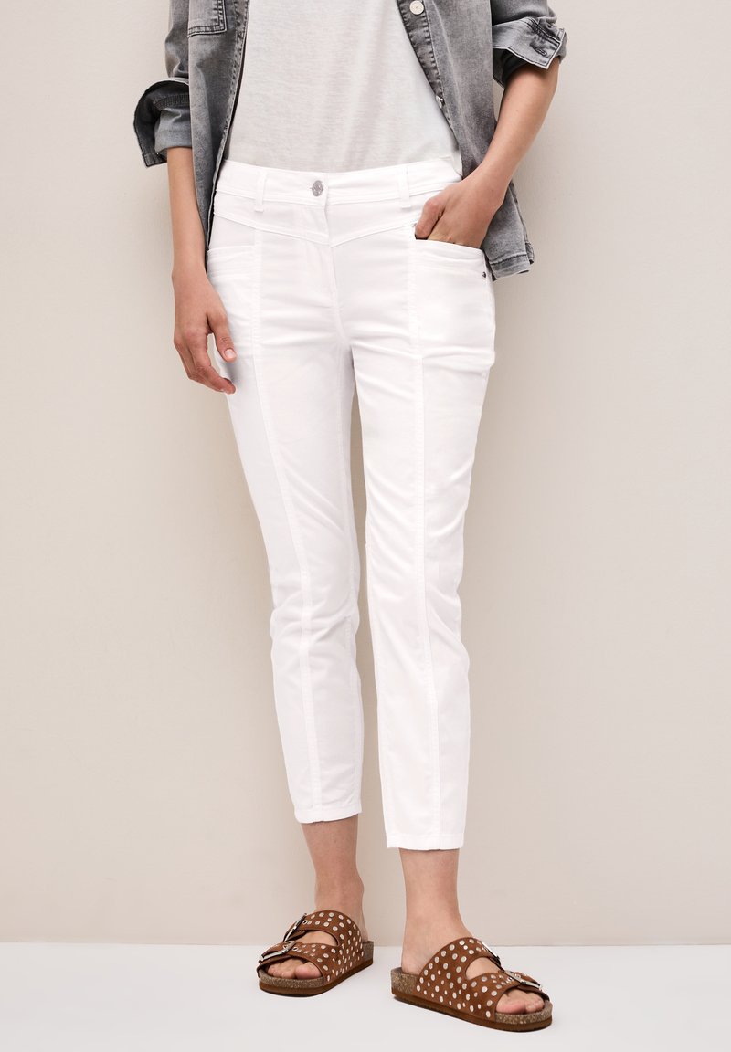 Pantalones cortos blancos con bolsillos frontales, con detalles de costura vertical. Combinados con sandalias marrón con lunares y una camisa gris.