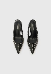 Chaussures à bride arrière noires avec bouts pointus, ornées de clous argentés le long des côtés. Texture cuir lisse avec un design élégant.