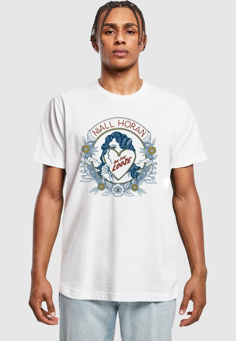 Hvid bomulds t-shirt med et farverigt trykt design, der viser en kvinde, der holder et hjerte, omgivet af blomsterlige elementer og tekst.