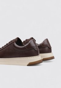 Zapatillas de cuero marrón con una superficie texturizada, con una suela de color crema, costuras sutiles y un diseño de perfil bajo.