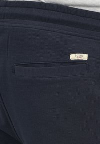 Tissu bleu marine avec une finition texturée, présentant une poche arrière et une étiquette indiquant "BLEND". Le design est simple et fonctionnel.