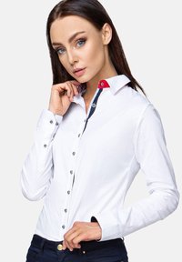 White long-sleeve shirt with a red accent on the collar, navy button details, and a fitted design, made of smooth fabric.