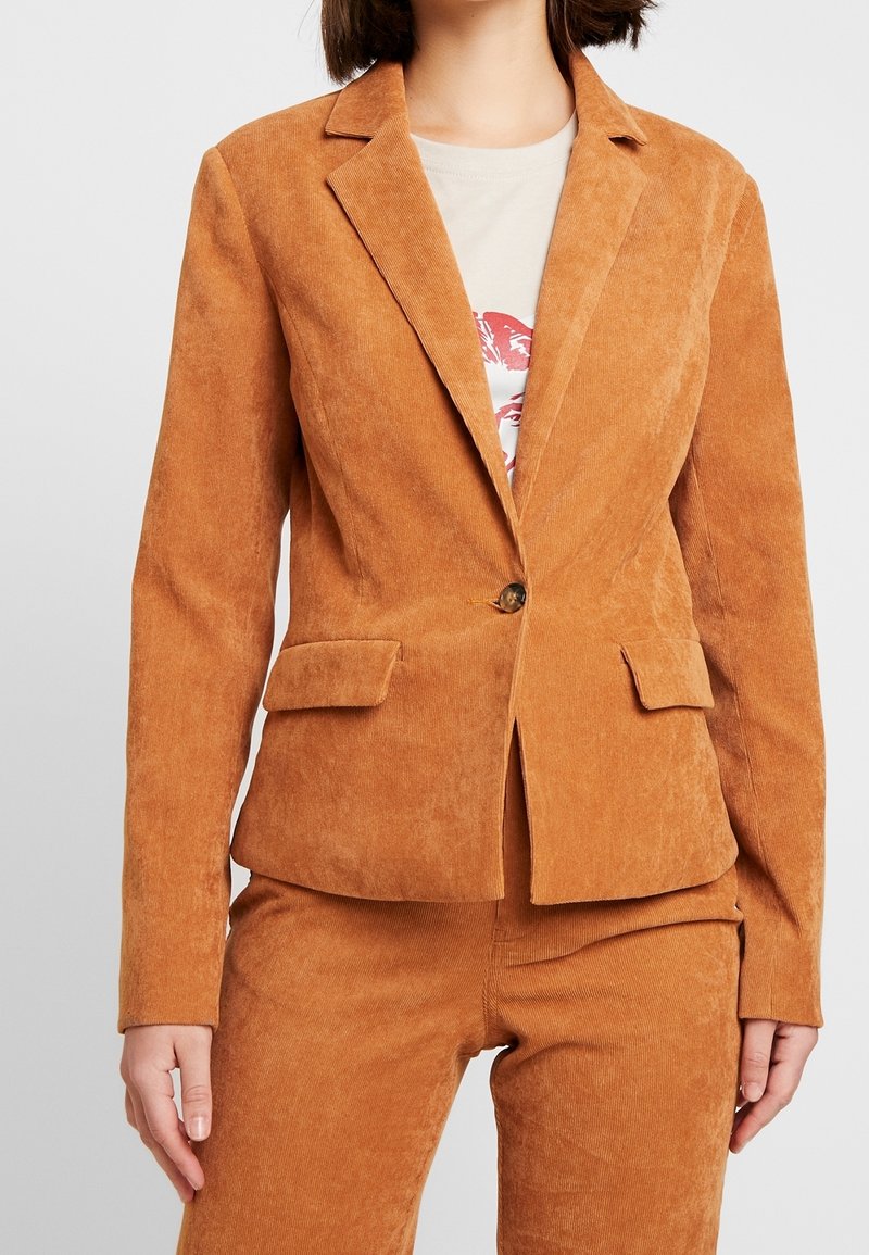 Kraftig orange kordflöjlsblazer med enkel knappstängning, slagna kragar, två framfickor och texturerad yta.