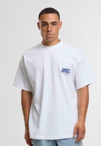 Valkoinen puuvillapaita, jossa on pyöreä kaula-aukko ja lyhyet hihat. Vasemmassa rinnassa sininen painettu logo. Sujuva, pehmeä materiaali ja rento istuvuus.