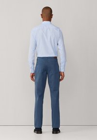 Jasnoniebieska koszula na guziki z długim rękawem, zestawiona z ciemnoniebieskimi spodniami. Slim fit, gładka faktura i minimalne detale.