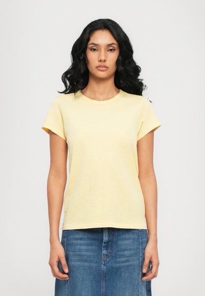 T-shirt jaune à manches courtes avec un col rond et une coupe décontractée, fabriqué en tissu doux. Associé à une jupe en denim bleue.