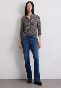 Camisa de botones con un diseño estampado, combinada con jeans acampanados azules y mocasines oscuros; tejido suave, silueta ajustada y piernas rectas.