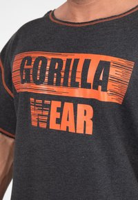 Grijze katoenen t-shirt met opvallende oranje tekst "GORILLA WEAR". Korte mouwen, ronde hals en contrasterende stikdetails. Zachte textuur.