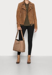 Hnědá semišová motorkářská bunda přes olivově zelenou dlouhý rukáv tričko, černé skinny džíny a hnědé kotníkové boty. Hnědá kabelka s přední kapsou.