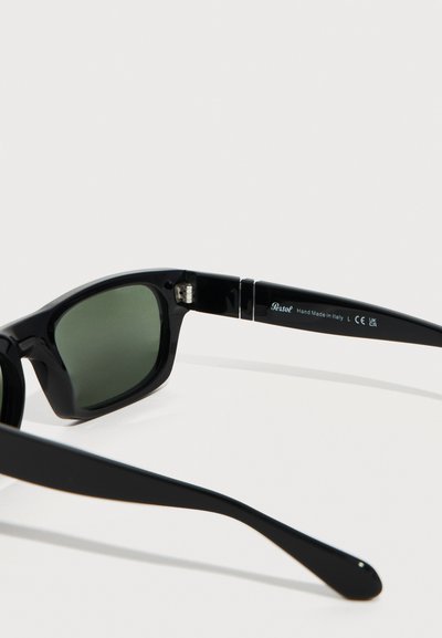 Μαύρα ορθογώνια γυαλιά ηλίου με πράσινους φακούς, σήμανση της μάρκας «Persol» και κείμενο «Κατασκευασμένα στο χέρι στην Ιταλία» στην εσωτερική πλευρά του βραχίονα.