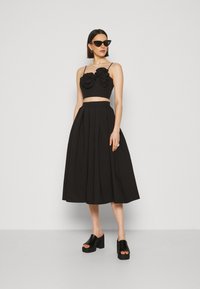 Fekete, virágmintás akcentusokkal díszített cropped top, amelyet egy magas derekú, redőzött fekete szoknyával párosítanak. Masszív fekete platform szandálok.