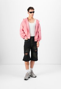 Pink cropped hoodie, hvid tanktop, slidte sorte jeanshorts, grå sneakers med hvide sokker, iført solbriller.