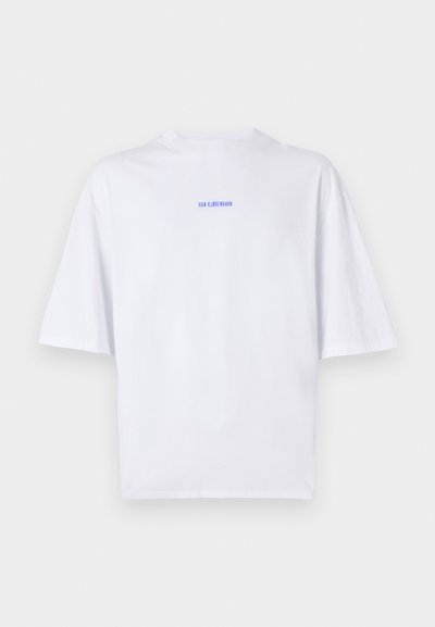 Bela bombažna majica oversize z kratkimi rokavi. Ima majhno modro besedilno oznako na hrbtu, minimalističen dizajn in gladko teksturo.