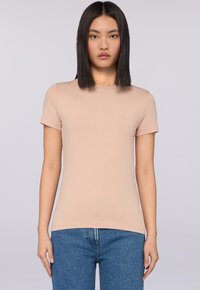 Jasnoróżowa koszulka z krótkim rękawem w dopasowanym fasonie, wykonana z miękkiego materiału, z subtelnym akcentem logo na klatce piersiowej.