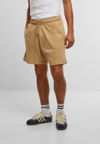 Khaki bomullsshorts med elastisk midjebånd og snøring, med sidelommer og subtile folder. Brukt med marineblå og kremfargede sneakers.