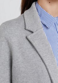 Grå ullblazer med strukturerade slag, textil med struktur, lagd över en blå och vit randig skjorta med klassisk krage.