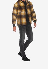 Struktureret gul- og brune plaidjakke med knaplukning, parret med en sort skjorte og mørkegrå jeans, båret med sorte ankelstøvler.