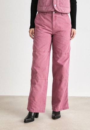 Roze, hoge taillebroek van katoen, met een ontspannen pasvorm, zichtbare stiksels en zijzakken, gecombineerd met zwarte haklaarzen.