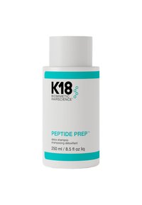 Witte cilindrische fles van K18 Peptide Prep detox shampoo. Heeft blauwe accenten, zwarte tekst en een verwijderbare dop. Bevat 250 ml.