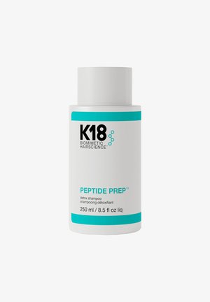 Witte cilindrische fles van K18 Peptide Prep detox shampoo. Heeft blauwe accenten, zwarte tekst en een verwijderbare dop. Bevat 250 ml.