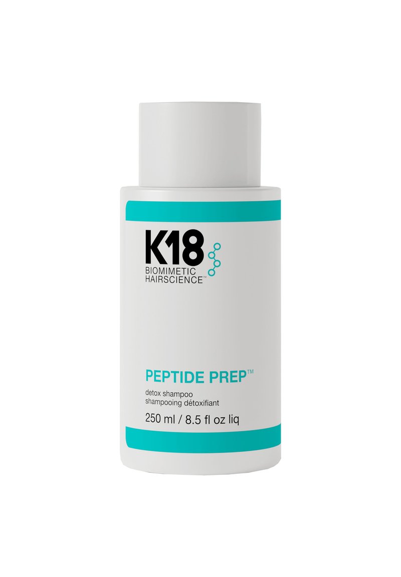 Witte cilindrische fles van K18 Peptide Prep detox shampoo. Heeft blauwe accenten, zwarte tekst en een verwijderbare dop. Bevat 250 ml.
