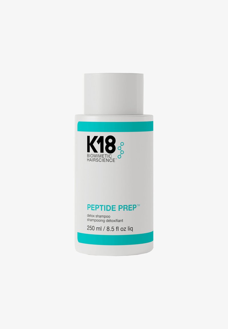 Witte cilindrische fles van K18 Peptide Prep detox shampoo. Heeft blauwe accenten, zwarte tekst en een verwijderbare dop. Bevat 250 ml.