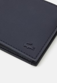Navy blue textured wallet with a smooth surface, featuring a subtle embossed logo and visible stitching along the edges.