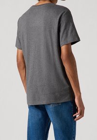 T-shirt en coton gris avec un col rond, des manches courtes, une coupe décontractée et une texture lisse, associé à un jean en denim bleu.