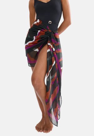 Kobieta ubrana w czarny jednoczęściowy strój kąpielowy oraz wielokolorowy sarong w czarne, fioletowe, białe i rdzawobrązowe wzory, związany w talii złotym pierścieniem.