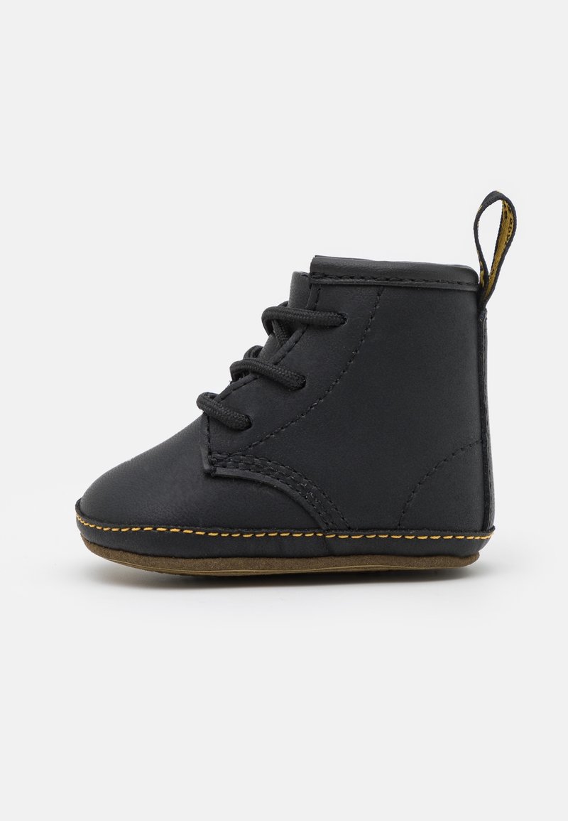 Bottine bébé en cuir noir avec lacets, coutures jaunes autour de la semelle, semelle souple et languette à l'arrière, montrée de profil sur fond blanc.