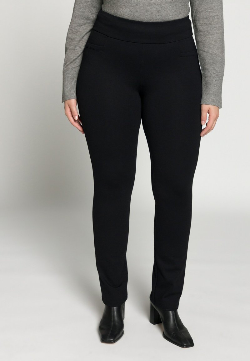 Schwarze Stretchhose mit hohem Bund, seitlichen Taschen, glatter Textur und schmal zulaufendem Bein, kombiniert mit schwarzen Stiefeln mit Absatz.