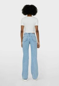 Camiseta blanca de algodón con textura y jeans de tiro alto de campana en azul claro. Bolsillos traseros desgastados y un corte relajado. Zapatillas blancas complementan el look.