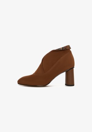 Bruine enkelboot met een spitse neus en hoge blokhak, voorzien van een gestructureerde patroonrand. Eenvoudig, elegant ontwerp op een witte achtergrond.