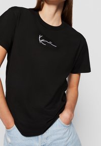 T-shirt en coton noir avec des manches courtes, un col rond, et un texte brodé en blanc sur la poitrine. Associé à un short en denim bleu clair.