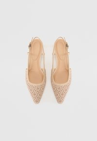 Paire d'escarpins slingback beige à bout pointu avec un motif géométrique tissé et des brides de cheville réglables sur fond blanc.