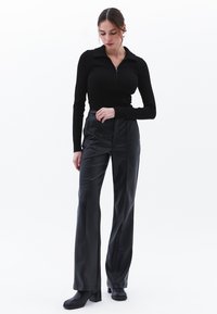 Musta pitkähihaine paita, jossa on vetoketjukaulus, yhdistettynä korkeavyötäröisiin mustiin housuihin, joissa on sileä pinta ja etusauman yksityiskohdat.