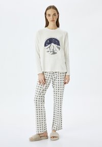 Top de manga larga color crema con un gráfico de montaña, combinado con pantalones de cuadros blancos y grises y zapatillas beige de felpa.