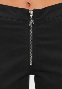 Pantalones de mezclilla negros con una cremallera plateada en la parte delantera, con un acabado texturizado y un diseño de corte recto. Los detalles incluyen un tirador de cremallera personalizado.