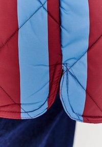 Prošívaná bunda s vínovými a světle modrými diagonálními pruhy, vyrobená z polyesterové látky, s kontrastním šitím na lemu.