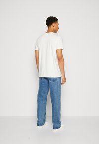 Weiße kurzärmlige T-Shirt aus Baumwolle, kombiniert mit lockeren blauen Jeans, die über Gesäßtaschen verfügen, getragen mit weißen Sneakers.