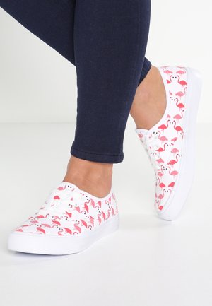 Zapatillas de lona blancas con un patrón de flamencos rosas, diseño de cordones y suela de goma blanca. Combinadas con unos vaqueros de denim azul oscuro.