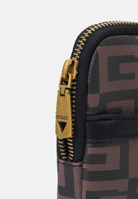 Il portafoglio in poliestere presenta un motivo geometrico in marrone e nero, arricchito da una zip dorata con un tirante marchiato. Finitura testurizzata e design compatto.