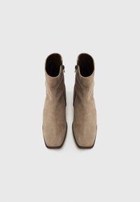 Paire de bottines en daim taupe avec bouts carrés et fermetures éclair sur le côté, vues de dessus sur un fond clair.