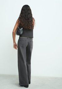 Vaqueros negros de pernera ancha y talle alto con tachuelas laterales, hechos de algodón y con un ajuste relajado. Combinados con un bolso negro de hombro y un top corto.