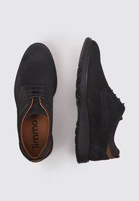 Chaussures en daim noir avec une finition lisse, bout rond, semelle plate en caoutchouc et accents en cuir brun autour du talon et de la languette.
