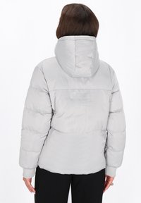 Lys grå pufferjakke med hætte, der har ribbede manchetter og et quiltet design. Glat tekstur og en tætsiddende silhuet ved taljen.