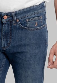 Jeans in denim blu scuro con vestibilità dritta, dotati di una tasca frontale, bottone di rame e un logo discreto ricamato sulla tasca posteriore.