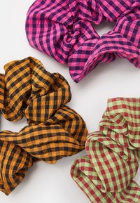 Três ganchos de cabelo em diferentes cores: xadrez rosa e roxo, xadrez preto e laranja, e xadrez verde e vermelho. Textura de tecido suave.