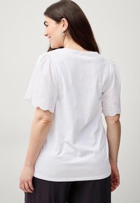 T-shirt bianco in cotone con maniche corte a sbuffo con bordi smerlati e dettagli in occhio di pernice, vestibilità casual e scollatura arrotondata.